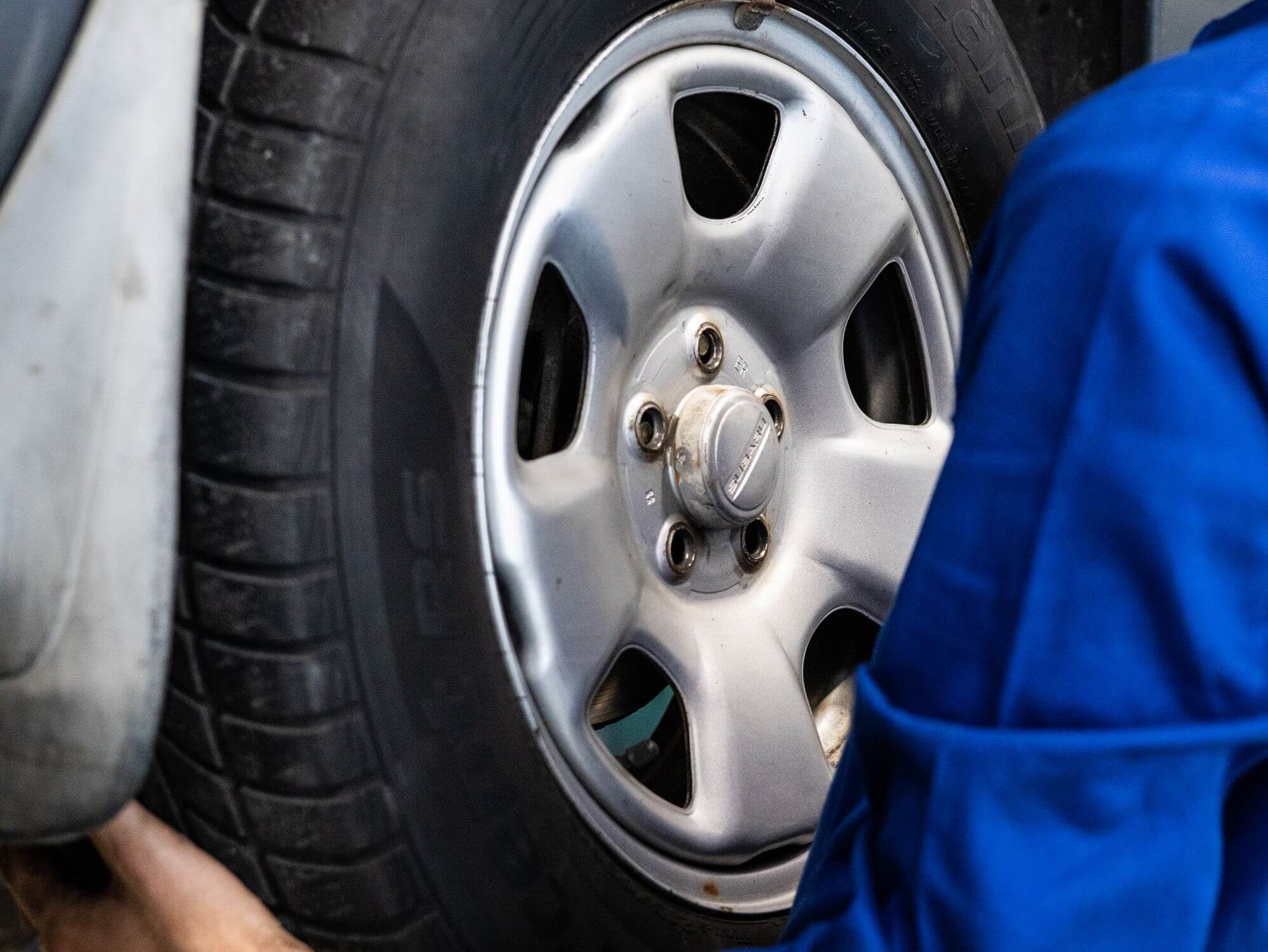 Mecánico revisando la rueda de un vehículo ilustrando los gastos obligatorios al mantener un coche o una moto